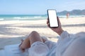 A woman holding white mobile phone with blank desktop screen while laying down on beach chair on the beach Royalty Free Stock Photo