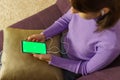 Mockup image of woman on sofa and holding mobile phone with headphones and blank green screen