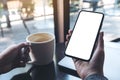 Mockup image of a woman`s hand holding black mobile phone with blank white desktop screen with coffee cup and laptop Royalty Free Stock Photo