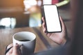 A woman`s hand holding black mobile phone with blank white desktop screen while drinking coffee with laptop on table in cafe Royalty Free Stock Photo