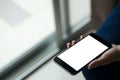 Mockup image of woman`s hand holding black mobile phone with blank white screen on thigh with white tile floor Royalty Free Stock Photo