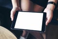 Mockup image of woman`s hand holding black tablet with blank white screen on thigh with wooden floor background Royalty Free Stock Photo