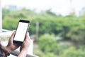 Mockup image of a woman`s hand holding and using black smart phone with blank white screen while standing at the balcony Royalty Free Stock Photo