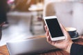 Mockup image of a woman`s hand holding white mobile phone with blank black desktop screen and laptop on wooden table Royalty Free Stock Photo