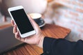 Mockup image of a woman`s hand holding white mobile phone with blank black desktop screen and laptop on wooden table Royalty Free Stock Photo