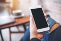 Mockup image of a woman`s hand holding white mobile phone with blank black desktop screen on thigh Royalty Free Stock Photo