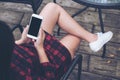 A woman`s hand holding white mobile phone with blank black screen on thigh with wooden floor background in vintage cafe Royalty Free Stock Photo