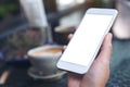 Mockup image of a woman`s hand holding white mobile phone with blank desktop screen and coffee cup