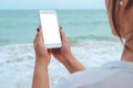 Mockup image of a woman`s hand holding white mobile phone with blank desktop screen by the sea and blue sky Royalty Free Stock Photo