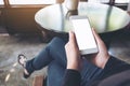 A woman`s hand holding white mobile phone with blank desktop screen on thigh in cafe Royalty Free Stock Photo