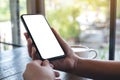 Woman`s hands holding black mobile phone with blank desktop screen with coffee cup on wooden table in cafe Royalty Free Stock Photo