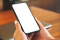 Woman`s hands holding black mobile phone with blank white screen with laptop computer on wooden table Royalty Free Stock Photo