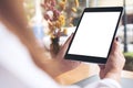 Woman`s hands holding black tablet pc with blank white desktop screen , laptop and coffee cup on wooden table in cafe Royalty Free Stock Photo