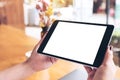 Mockup image of woman`s hands holding black tablet pc with blank white desktop screen , laptop and coffee cup on wooden table Royalty Free Stock Photo