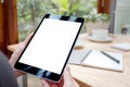 A woman`s hands holding black tablet pc with white blank screen with notebook and coffee cup on table Royalty Free Stock Photo