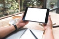 A woman`s hands holding black tablet pc with white blank screen with notebook and coffee cup on table Royalty Free Stock Photo