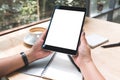 A woman`s hands holding black tablet pc with white blank screen with notebook and coffee cup on table Royalty Free Stock Photo