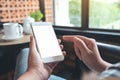 A woman`s hands holding and pointing at white mobile phone with blank screen with coffee cup on table in modern cafe Royalty Free Stock Photo