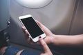 Woman`s hands holding and pointing at a white smart phone with blank black desktop screen next to an airplane window Royalty Free Stock Photo