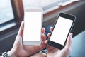 A woman`s hands holding two mobile phones with blank white screen in modern cafe