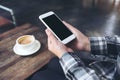 A woman`s hands holding white mobile phone with blank black desktop screen with coffee cup on wooden table in cafe Royalty Free Stock Photo