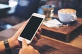 A woman`s hands holding white mobile phone with blank black screen with coffee cup , tea and snack on wooden table in vintage cafe Royalty Free Stock Photo