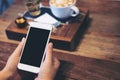 A woman`s hands holding white mobile phone with blank black screen with coffee cup , tea and snack on wooden table in vintage caf Royalty Free Stock Photo