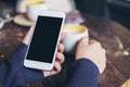 Woman`s hands holding white mobile phone with blank black screen and a coffee cup on wooden table in vintage cafe Royalty Free Stock Photo