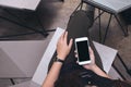 Woman`s hands holding white mobile phone with blank black screen on thigh in modern loft cafe Royalty Free Stock Photo