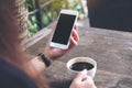 Mockup image of woman`s hands holding white mobile phone with blank black screen and white coffee cup Royalty Free Stock Photo