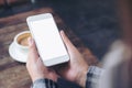 A woman`s hands holding white mobile phone with blank desktop screen with coffee cup on wooden table in cafe Royalty Free Stock Photo