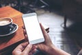 A woman`s hands holding white mobile phone with blank desktop screen with coffee cup on wooden table in cafe Royalty Free Stock Photo