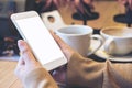 Woman`s hands holding white mobile phone with blank screen and white coffee cup in modern loft cafe Royalty Free Stock Photo