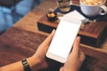 A woman`s hands holding white mobile phone with blank screen with coffee cup on wooden table in vintage cafe Royalty Free Stock Photo