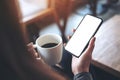 A woman sitting cross legged , holding black mobile phone with blank white desktop screen on thigh while drinking coffee in cafe Royalty Free Stock Photo