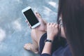 Mockup image of a woman sitting crossed leg and holding white mobile phone with blank black screen with concrete floor Royalty Free Stock Photo