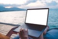 Mockup image of a woman using laptop with blank white desktop screen while sitting by the sea Royalty Free Stock Photo