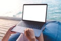 Mockup image of a woman using laptop with blank white desktop screen while sitting by the sea Royalty Free Stock Photo