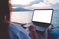 Mockup image of a woman using laptop with blank white desktop screen while sitting by the sea Royalty Free Stock Photo