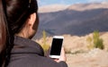 Mockup image of a woman using white mobile phone with blank black screen while standing in front of mountain Royalty Free Stock Photo