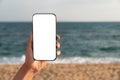 Mockup image of a woman& x27;s hand holding a white mobile phone screen against a background of blue sky, sea and beach Royalty Free Stock Photo