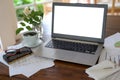 Mockup, laptop with blank white screen on a wooden desk with papers, glasses and a coffee cup, business workspace in a home office