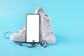 Mockup mobile cellphone with blank screen, earphone and running shoes on blue background. Healthy lifestyles