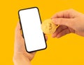 Mockup pay with bitcoin, yellow background, woman with mobile phone and golden coin in hands, copy space