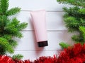 Mockup of pink squeeze bottle plastic tube with black cap, fir / pine borders and red garland on white wooden table. Bottle for