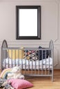 Mockup poster in black frame on the grey wall of baby room interior with crib with pillows, vertical view Royalty Free Stock Photo