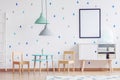poster in black frame, pastel colored lamps and wooden furniture in bright kid`s playroom interior