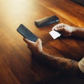 Mockup shot of man`s hand with tattoos holding  cell phone and credit card with blank screen on desk at home office. For shopping Royalty Free Stock Photo