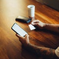 Mockup shot of man`s hand with tattoos holding  cell phone and credit card with blank screen on desk at home office. For shopping Royalty Free Stock Photo