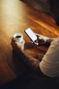 Mockup shot of man`s hand with tattoos holding a coffee cup and cell phone with blank screen on desk at home office Royalty Free Stock Photo